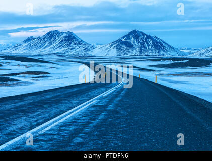 Straße auf der schneebedeckten Berge in der Abenddämmerung im Winter schneebedeckten Gipfel. Der Ring Road (Route 1) von Island, zwischen Greymouth und Akureyri. Natürliche Landsc Stockfoto