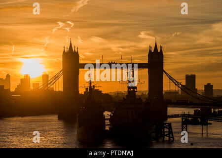 London, Großbritannien. 9. Okt. 2018. Die Sonne geht ofer Tower Bridge und HMS Belfast als Menschen pendeln in die Arbeit über London Bridge. Credit: Guy Bell/Alamy leben Nachrichten Stockfoto
