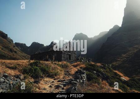 Santo Antao, Kap Verde - Jan 5 2016: verlassene Gebäude mitten in eines der Täler bei Sonnenuntergang mit gelben Gras, hohen Klippen und Gott Ra Stockfoto