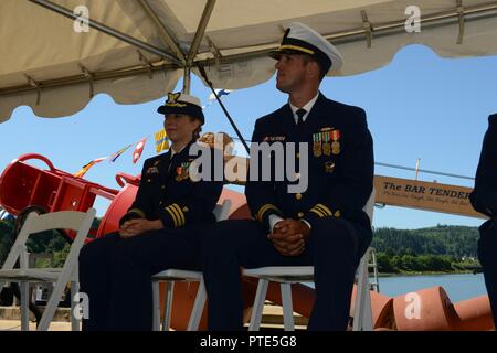 Cmdr. Kristen Serumgard, kommandierender Offizier Coast Guard Cutter Tanne und Lt.Cmdr. Jason Haag sitzen vor der 225-Fuß-Juniper Klasse seegängige tender Spitznamen "der Barkeeper" während des Fir Ändern des Befehls Zeremonie an der Unterseite der Zunge Punkt in Astoria, Erz, 14. Juli 2017 Boje. Haag entlastet Serumgaard als Kommandierender Offizier der Tanne und übernahm das Kommando der Cutter und Besatzung verantwortlich für die Wartung der Navigationshilfen, die Markierung der sicheren Navigation tv entlang der Küsten von Oregon und Washington. Us-Küstenwache Stockfoto