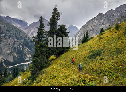 Zwei Touristen mit Rucksäcken zu Fuß auf den Weg in den Berg Tal bei bedecktem Himmel Hintergrund. Reisen Abenteuer Konzept Stockfoto