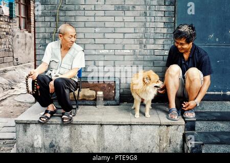 Peking/China - 24.Juni 2011: zwei Mann spielt mit einem Hund außerhalb ihres Heimatlandes in einem traditionellen chinesischen Stadt Hutong Stockfoto