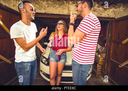 Eine Gruppe von zwei Jungen und ein Mädchen, lächeln und Spaß neben einem Parkplatz weißes Auto und runining Garage Stockfoto