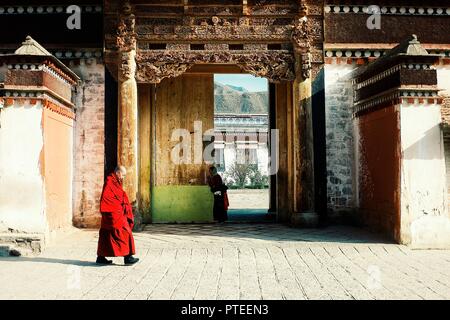 Labrang Monastery, Xiahe, Gansu Provinz/China - Aug 6 2011: ein tibetischer Mönch vorbei gehen von einem der Tempel während ein Pilger betende Frau im b Stockfoto