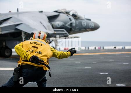 U.S. Navy Petty Officer 1st Class Juan F. Coello, einer Luftfahrt Bootsmann Mate's (Handling) zugeordnet die Amphibisches Schiff USS Wasp (LHD-1), ein AV-8B Harrier Pilot, Marine Attack Squadron (VMA) 231 zugeordnet, auf dem Flugdeck des Wasp während des Fluges Zertifizierung Operationen, 16. Juli 2017. VMA-231 die Wespe in den Erwerb Flug Zertifizierungen in der Vorbereitung für die bevorstehende homeport Verschiebung nach Sasebo, Japan, wo Sie sind schiefergedeckt, die USS BONHOMME RICHARD (LHD 6) in der 7.Flotte Einsatzgebiet zu entlasten unterstützt. Stockfoto