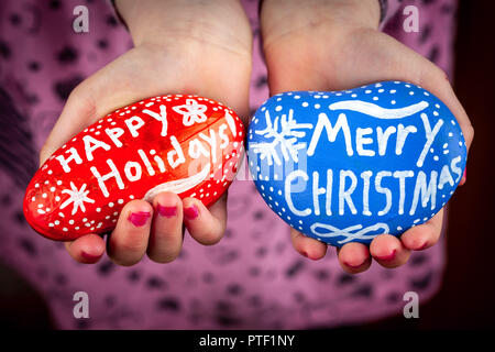 Girl Holding gemalt Felsen mit frohe Feiertage und Frohe Weihnachten Schriftzug closeup Stockfoto