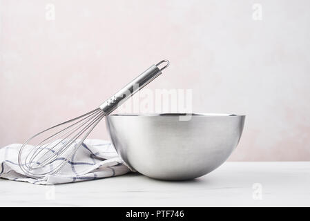 Backen Konzept. Schüssel mit einem Schneebesen und Geschirrtuch auf weißem Marmortisch über rosa Hintergrund mit kopieren. Stockfoto
