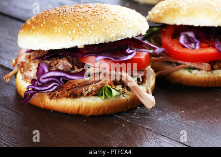 Gezogene Schweinefleischsandwiche mit BBQ Sauce, Kohl und Tomaten auf dem Tisch. Stockfoto