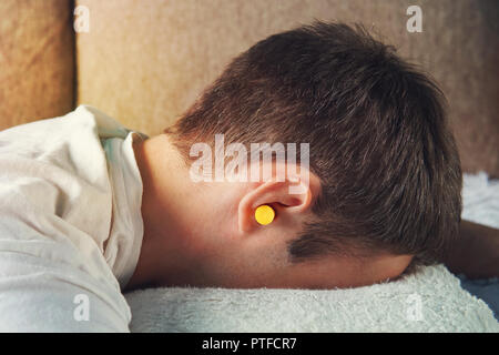 Schöne junge Mann schlafen, in die Ohren gelben Ohrenstöpsel gegen Straßenlärm, Rettung von der lauten Nachbarn. wenn Schlaf verhindern. Stockfoto