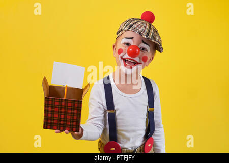 Funny kid Clown auf gelbem Hintergrund. Schönen verspielten portrait Kind Junge Narren in Make-up. Ausdruck Gesicht Freude, Lächeln, Spaß, fröhlich. 1 April Fool's Day Konzept. Stockfoto