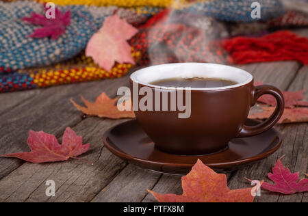 Dampfende Tasse Kaffee auf einem urigen Holz- Oberfläche mit Herbst Blätter und bunte Decke im Hintergrund Stockfoto