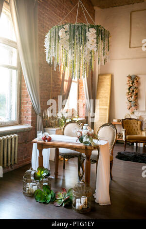 Esstisch mit Stühlen, Blume, Kronleuchter, Früchte und Sukkulenten in Dachboden mit Blumen Stockfoto
