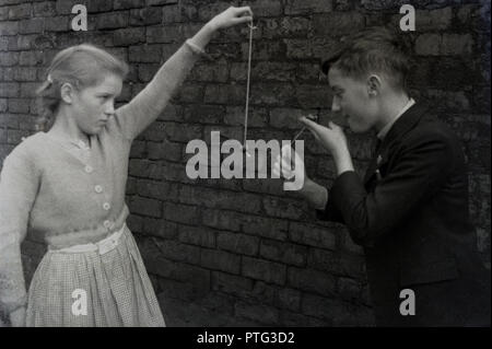 1940er Jahre, ein Junge und ein Mädchen in einem Straße Spielen ist ein traditionelles Kinder Spiel der CONKERS, England, UK. Der harte Samen der Rosskastanie Baum, die Spieler haben jeweils eine conker (Samen) am Ende ein Stück Schnur und abwechselnd versuchen zu knacken ein Gegner conker Pause oder. Stockfoto