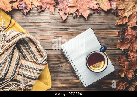 Herbst Mode saisonale Konzept gelb warm weicher Pullover skandinavischen Strickschal Tasse heißer schwarzer Tee Kaffee Fallen gefallen Ahornblätter auf Holztisch mit Notebook pen. Flach Top view Vintage Style Stockfoto
