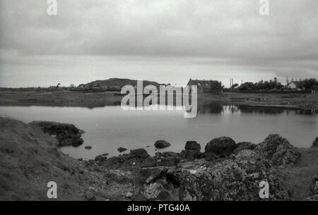 1950, historische, Blick auf eine kleine Kirche und ein Häuschen durch eine natürliche Bucht auf den Äußeren Hebriden, Western Isles, Schottland, Großbritannien. Stockfoto