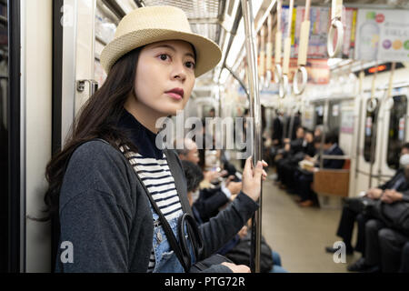 Eine Frau trägt einen Strohhut, die U-Bahn, viele Geschäftsleute im Anzug im Hintergrund sitzen Stockfoto