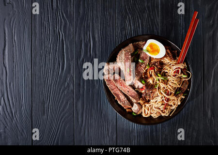 Soba Nudeln mit in Scheiben geschnittenen Rinderbraten, Shiitake-Pilze, gekochte Eier und gebratenes Gemüse in eine Schüssel geben. Dunkle essen Fotografie. Ansicht von oben Stockfoto