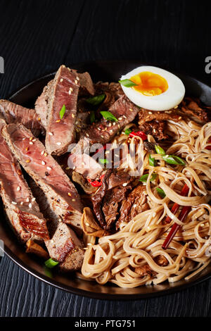 Close-up schwarz Schüssel Soba Nudeln mit in Scheiben Roastbeef, Shiitake-pilze, die Hälfte der hart gekochten Ei und gebratenem Gemüse mit Stäbchen, asiatische Stockfoto