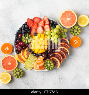 Rohe Früchte Beeren Platter, Mango, Orangen, Kiwi, Erdbeeren, Heidelbeeren, Trauben Grapefruit auf die weiße Platte, an der aus weißer Tisch, quadratisch, oben Stockfoto