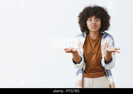 Was wollen Sie mir sagen. Verzweifelt, traurig und düster african american Female in transparenten Gläser mit lockigem Haar, Palmen in der Nähe der Brust in ratlos und verwirrt Geste kann nicht verstehen, warum Stockfoto