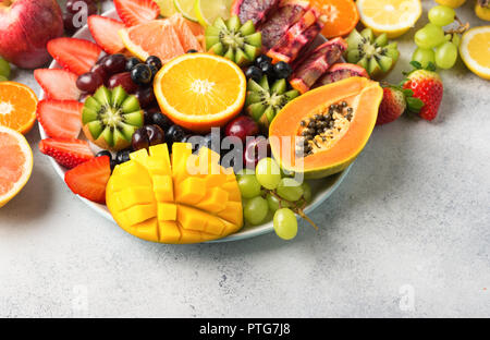Auswahl der rohen Früchte Beeren, Mango, Orangen, Kiwi, Erdbeeren, Blaubeeren grapefruit Trauben, Bananen, Äpfel auf dem weißen Teller, auf dem Weg von whit Stockfoto