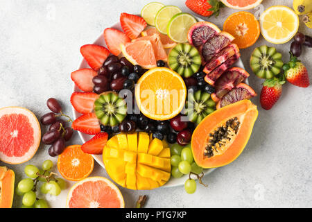 Rohe Früchte Beeren Platter, Mango, Orangen, Kiwi, Erdbeeren, Blaubeeren grapefruit Trauben auf die weiße Platte, an der aus weißen Tabelle, Ansicht von oben, cop Stockfoto