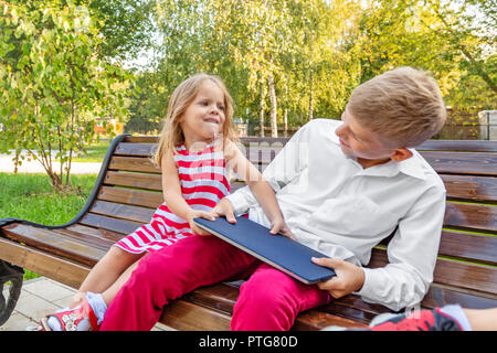 Bruder und Schwester im Park auf einer Bank nehmen einen Laptop von jedem anderen