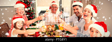 Zusammengesetztes Bild der Familie in Santas Hüte Toasten Weingläser am Esstisch Stockfoto