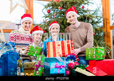 Mama, Papa und Söhne auf X-mas bei der Übergabe der Geschenke unter dem Weihnachtsbaum Stockfoto