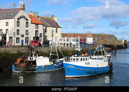 Menschen auf der Uferstraße von Eyemouth Hafen beobachten, ein kleines Fischerboot im Hafen in der Vergangenheit bereits ein anderes Schiff am Kai gebunden. Stockfoto