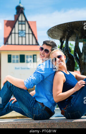 Glückliches junges Paar mit Sonnenbrille zurück sitzen in der Nähe der Brunnen zu zurück Stockfoto