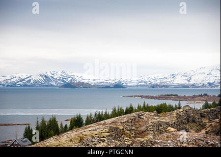 See Thingvallavatn, den Nationalpark Thingvellir, Island. Vulkanische Landschaft, Schnee bedeckte Bergkette, mit bunten Rock Risse im Vordergrund Stockfoto