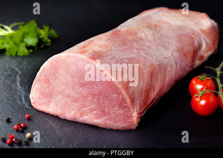 Rohes Fleisch und frisches Schweinefleisch. Schwarzer Hintergrund Roll Fleisch saftiger Schweinebraten mit Kirschtomaten Schiefer Stockfoto