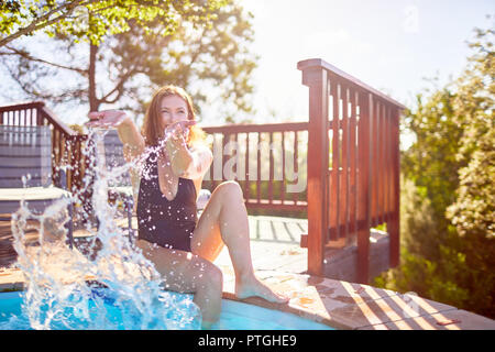 Verspielte junge Frau Spritzwasser am sonnigen Pool Stockfoto