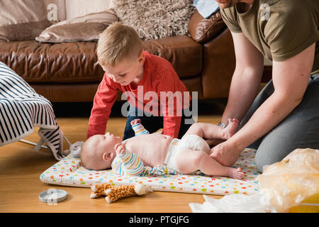 Kleinen Jungen helfen, sein Vater seinen Bruder ändern. Sie sind beide auf dem Boden saß im Wohnzimmer. Stockfoto