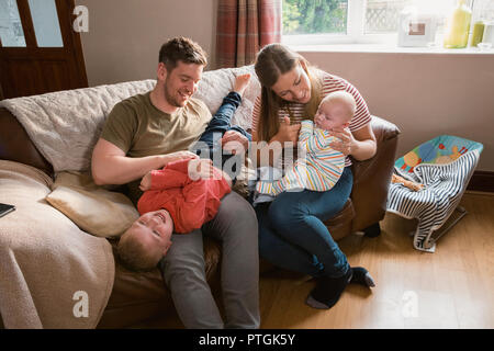 Familie von vier Sitzen auf dem Sofa in Ihrem Wohnzimmer. Ein Sohn wird tickeled von seinem Vater und sie lachen. Die Mutter sitzt auf den e Stockfoto