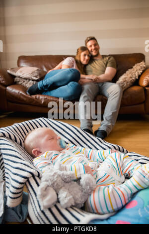Der Mann und die Frau sitzen, fernsehen und genießen Sie Ruhe und Frieden, während Ihr neugeborenes Baby schläft ein Baby Bouncer. Stockfoto