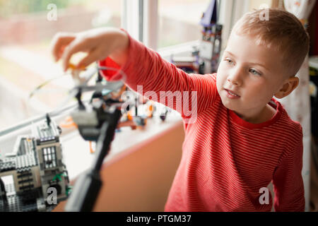 Kleiner Junge in einem gestreiften T-Shirt spielen mit Spielzeug in seinem Zimmer. Sie hat sich den Arm gedehnt bis zu Ort und Balace etwas während des Spielens. Stockfoto