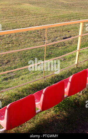 Drei Leere, rote Sitze mit Fußballplatz im frühen Herbst Stockfoto