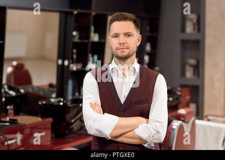 Stattlich und schweren Friseur tragen in weißem Hemd und Weste, posieren. Der Gesichtsausdruck der männlichen Friseur auf Kamera. Professionelle und zuversichtlich Master in Barbershop. Stockfoto