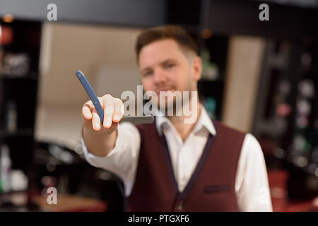 Nahaufnahme von Razor in die Hände der Friseur posieren für den Hintergrund. Männliche Friseur an Kamera suchen und halten Instrument für das Rasieren von Haaren. Konzept der Barbershop und Styling der Haare. Stockfoto