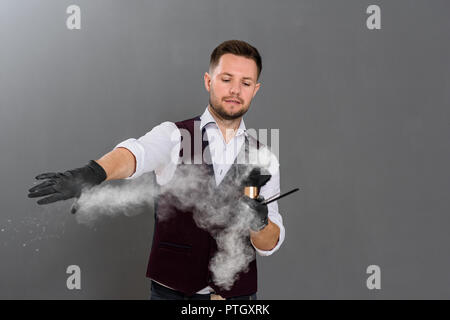 Stattliche Friseur im Studio auf grauem Hintergrund posiert. Männliche Friseur holding Instrumente für Haarschnitt und Pinsel, er verschüttet Pulver in der Luft. Master tragen weiße Classic Shirt und Weste. Stockfoto