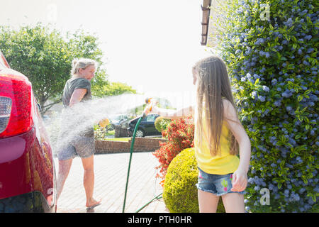 Verspielte Tochter spritzen Mutter mit Schlauch im sonnigen Auffahrt Stockfoto