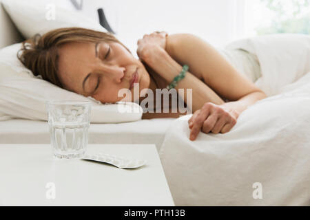 Ältere Frau schlafen im Bett mit Wasser und Medizin auf dem Nachttisch Stockfoto