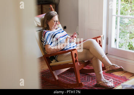 Ältere Frau sms mit Smart Phone im Schaukelstuhl Stockfoto