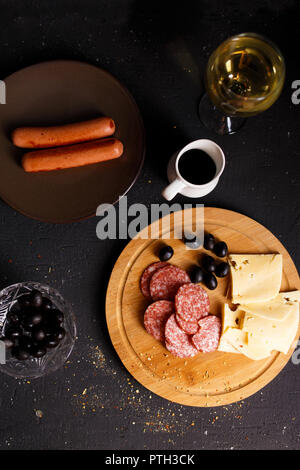 Charcuterie, gegrillte Würstchen, Käse, Salami, Pflaume Oliven und einem Glas Wein auf einem dunklen Tabelle Ansicht von Oben Stockfoto