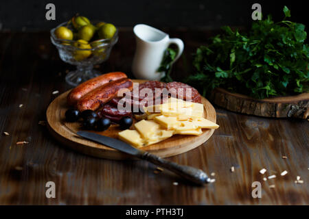 Aperitif Tabelle Fleisch Snack, gebratene Würstchen, Käse, Salami, Oliven und ein Glas Wein auf einem dunklen Menü Tabelle und Restaurant Konzept Stockfoto