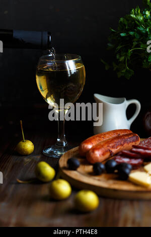 Aperitif. Der Wein fließt in einen Glas Becher. Auf dem Tisch, Fleisch Vorspeisen, gebratenen Würste, Salami, Käse, Oliven. Menü und Restaurant Konzept Stockfoto