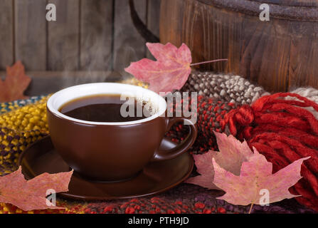 Dampfende Tasse Kaffee mit Herbstlaub auf einem bunten Decke Stockfoto
