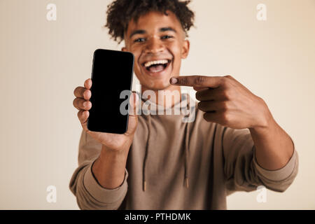 Porträt eines lächelnden jungen afro-amerikanische Mann in Hoodie isoliert gekleidet, zeigen auf Blank Screen Handy Stockfoto
